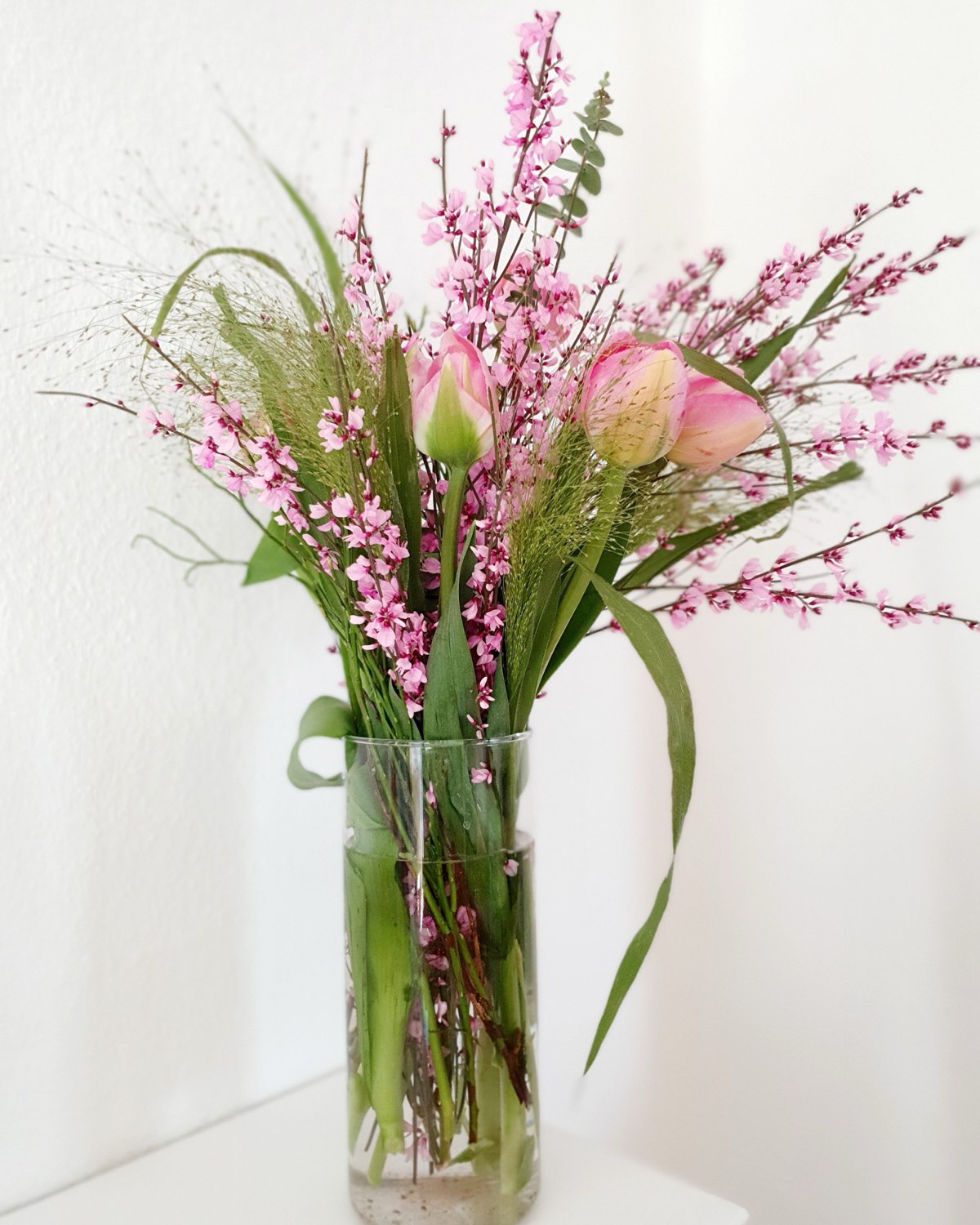 Tulpen und rosa Blütenzweige in einer Glasvase